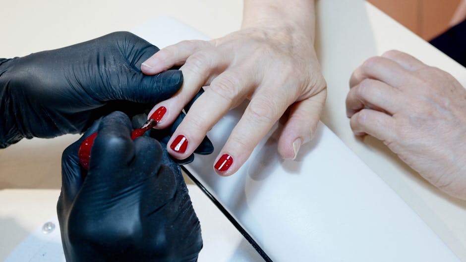 Close-up of a manicurist applying red nail polish to a customer's nails at a salon.
